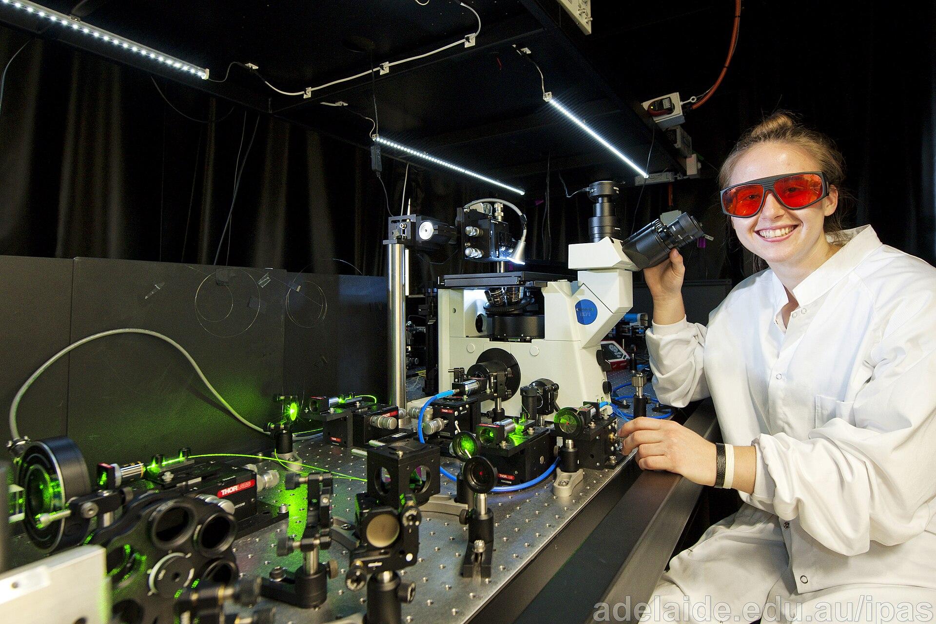 A researcher wearing protective glasses works beside a microscope and optical equipment at IPAS.