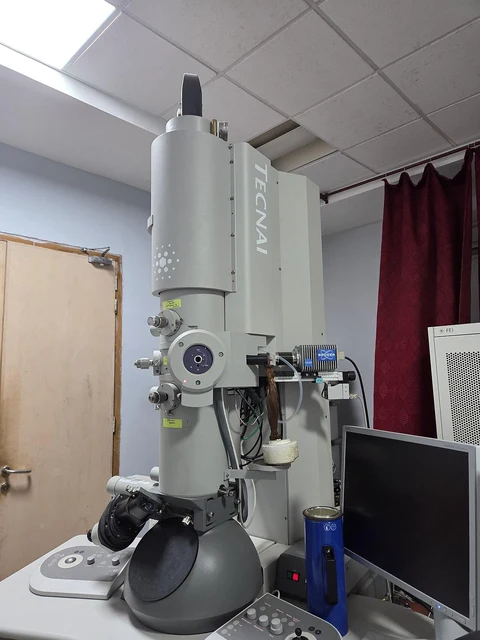 A tall transmission electron microscope with its control equipment in a laboratory.