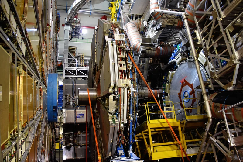 Detector modules, silver pipes and yellow access stairs inside the ATLAS cavern at CERN.