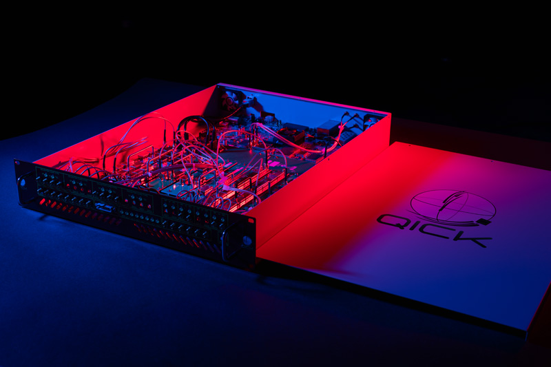 An open QICK electronics enclosure with densely connected circuit boards under red and blue lighting.