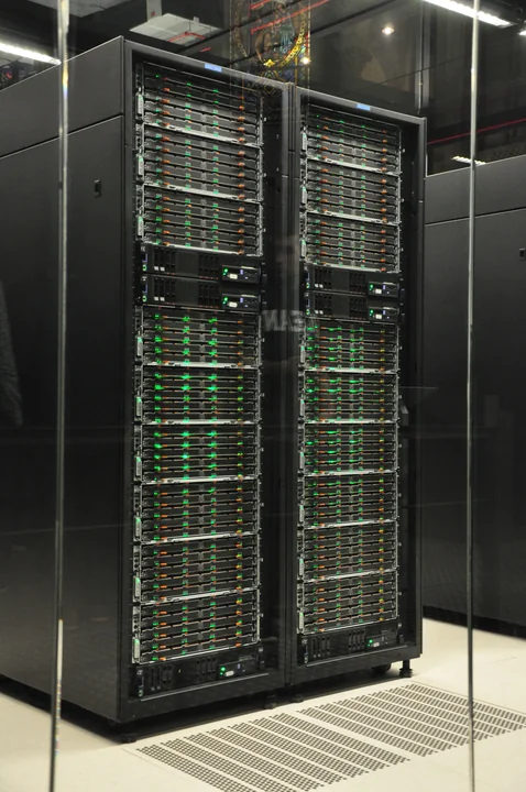 Two tall black racks of IBM server and storage equipment behind glass at Barcelona Supercomputing Center.