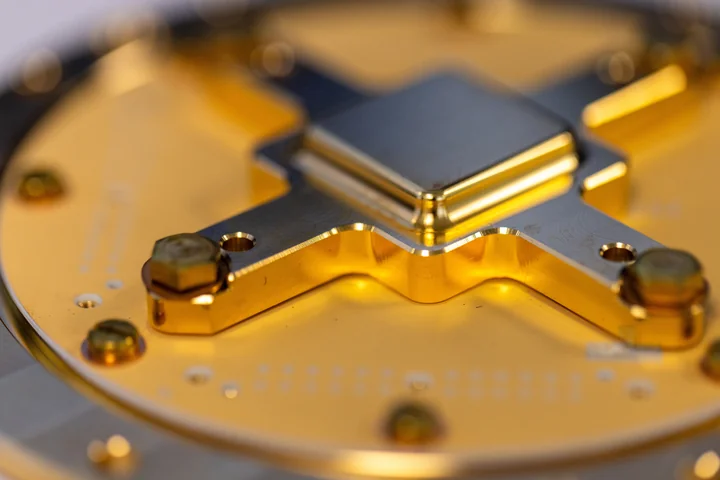 A dark square device is secured to a gold-colored mount with a metal retaining frame.