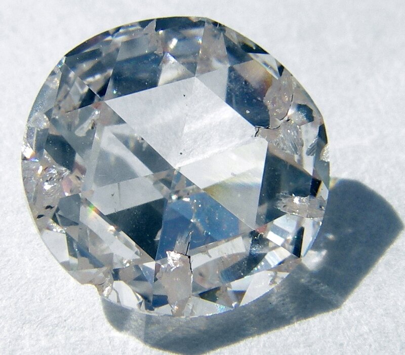 A clear rose-cut synthetic diamond on a pale surface.