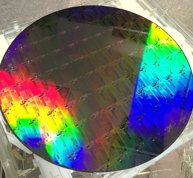 A circular silicon photonics wafer reflecting a spectrum of vivid colours.