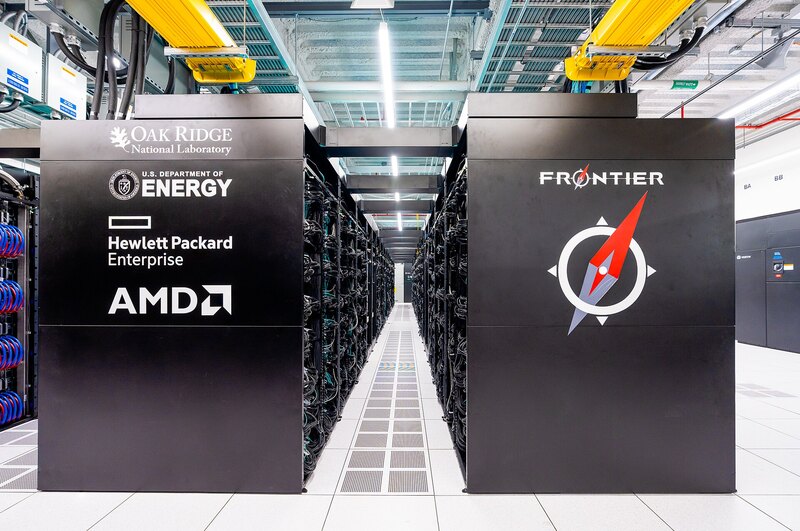 A brightly lit aisle between black Frontier supercomputer cabinets at Oak Ridge National Laboratory.