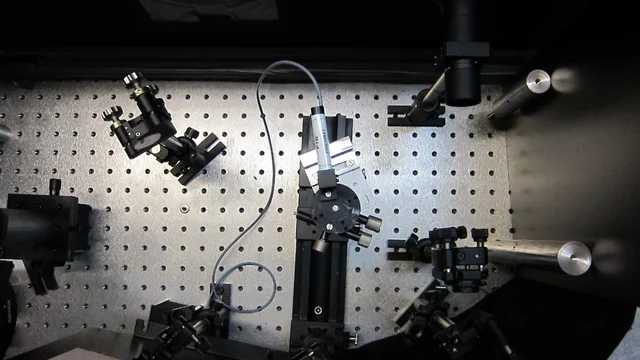 Top-down archival photograph of an optical table with mirrors, mounts, lenses and cables.