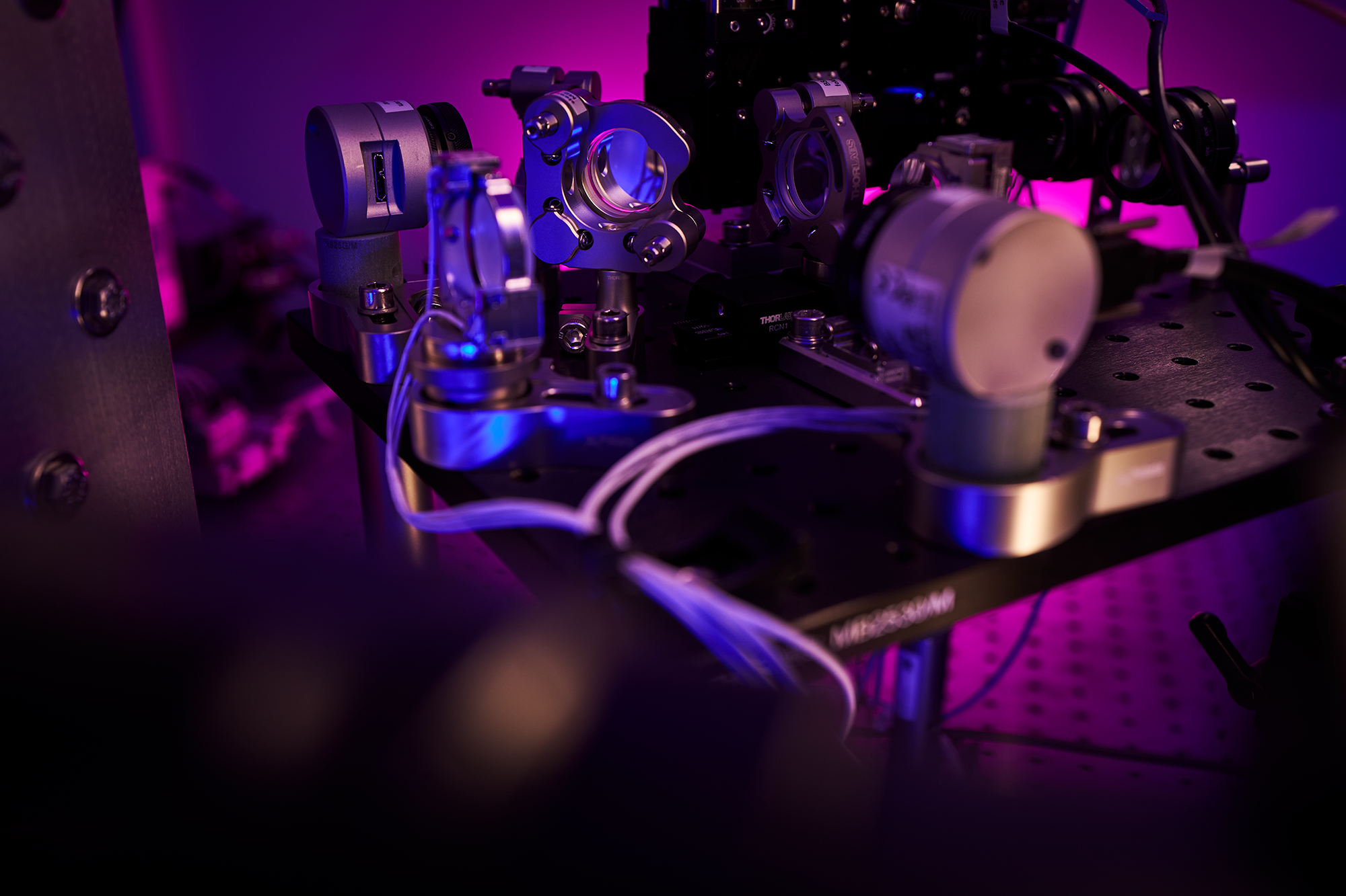 Optical components, mounts and cables inside the JION trapped-ion quantum computer under violet light.