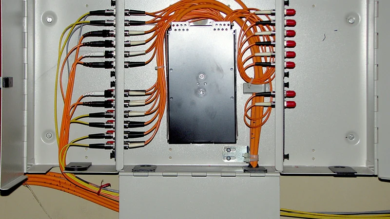 Orange fiber-optic cables loop between rows of connectors inside an open metal optical distribution cabinet.