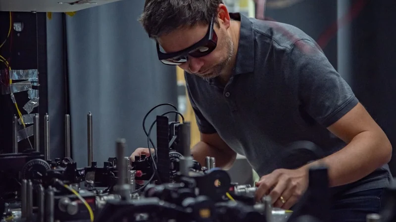 NIST physicist Krister Shalm wearing laser safety glasses while adjusting optical components on a laboratory bench.