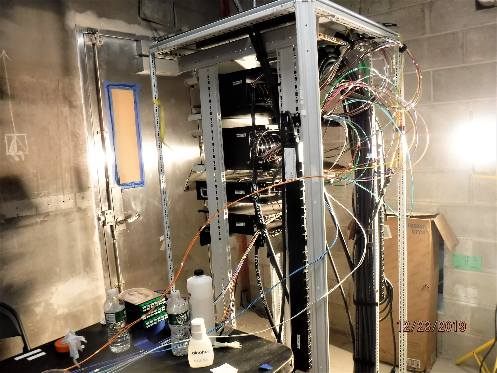 Colored fiber-optic strands hang from a communications rack during installation in a concrete-walled equipment room in Queens.