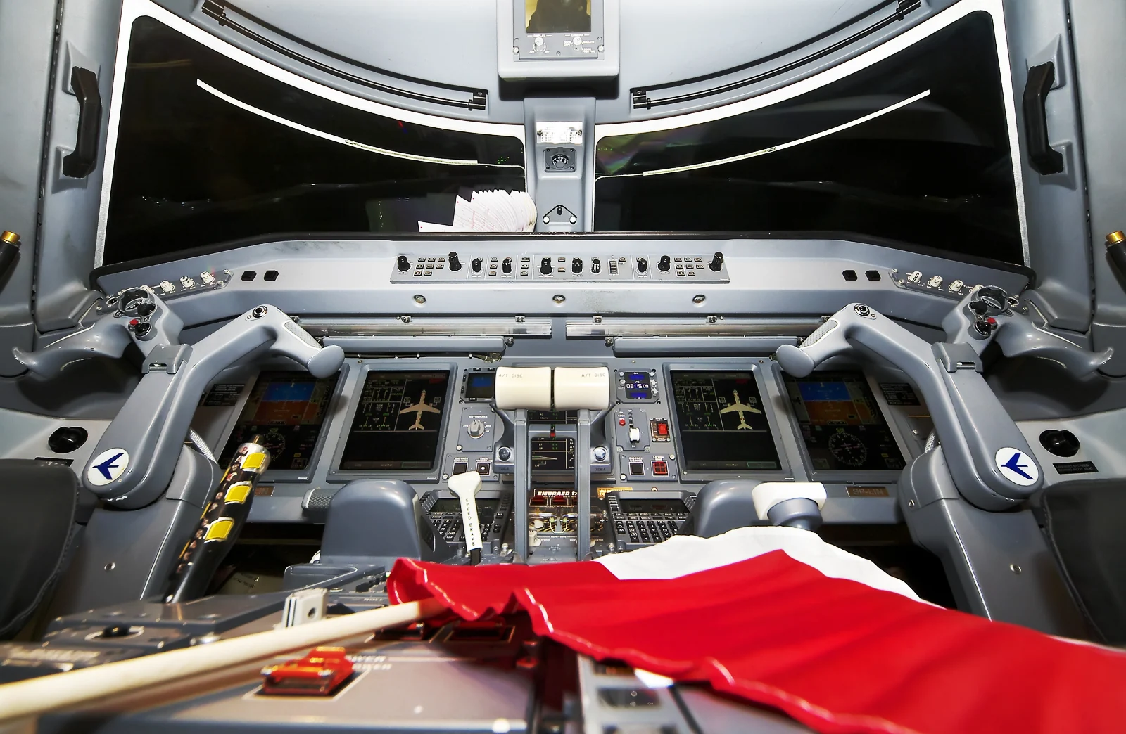 Two control yokes, illuminated flight displays and throttle controls in a LOT Embraer E175 cockpit.