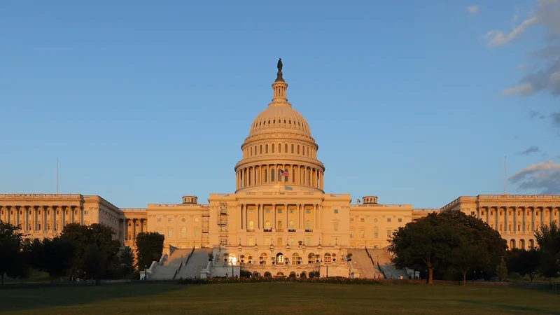 The illuminated west facade and dome of the United States Capitol beneath a blue dusk sky.