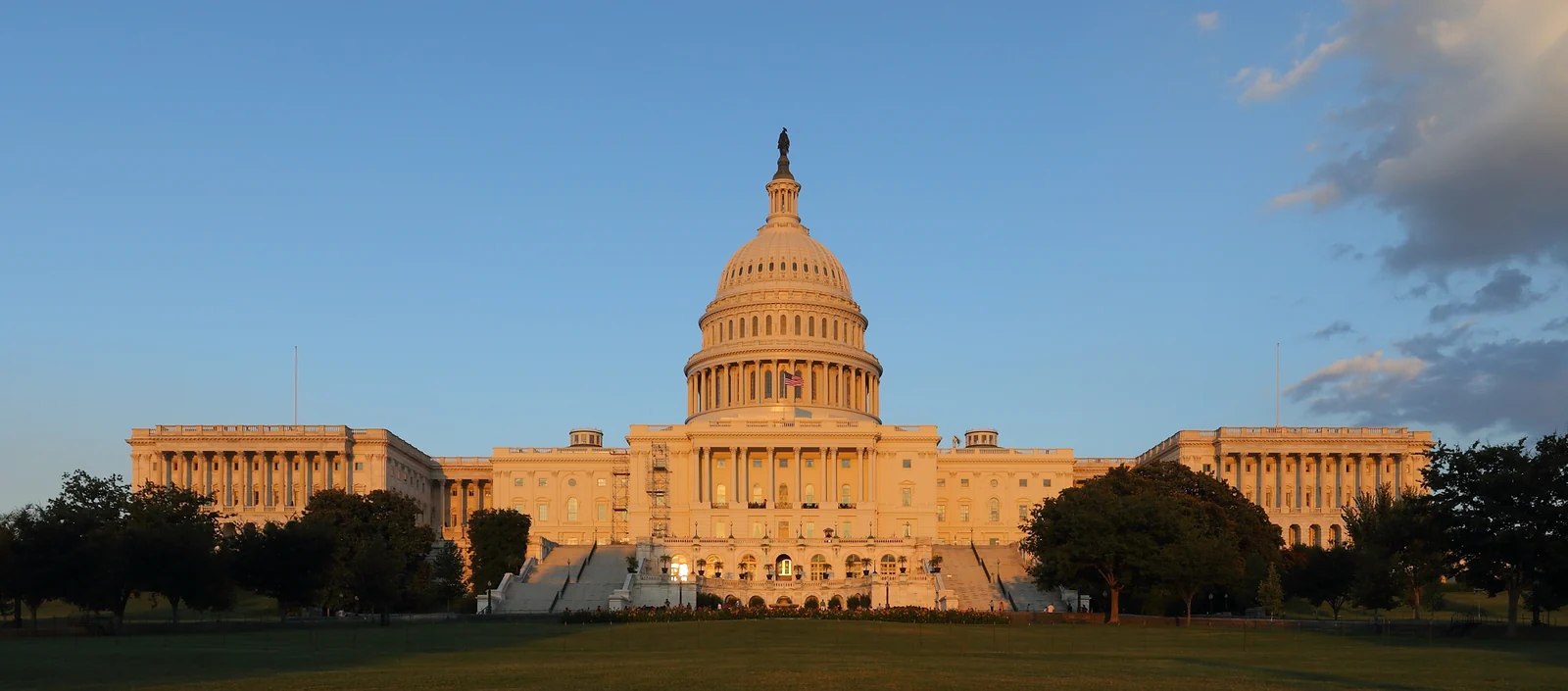 The illuminated west facade and dome of the United States Capitol beneath a blue dusk sky.