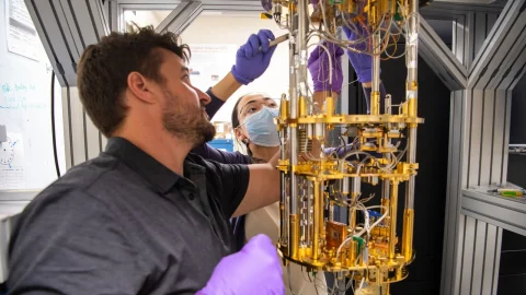 Christian Boutan and Jihee Yang adjust a gold-colored dilution refrigerator in a PNNL quantum laboratory