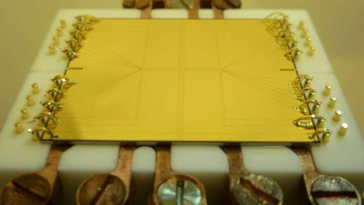 Gold-coloured atom chip mounted on a holder with fine electrical connections.