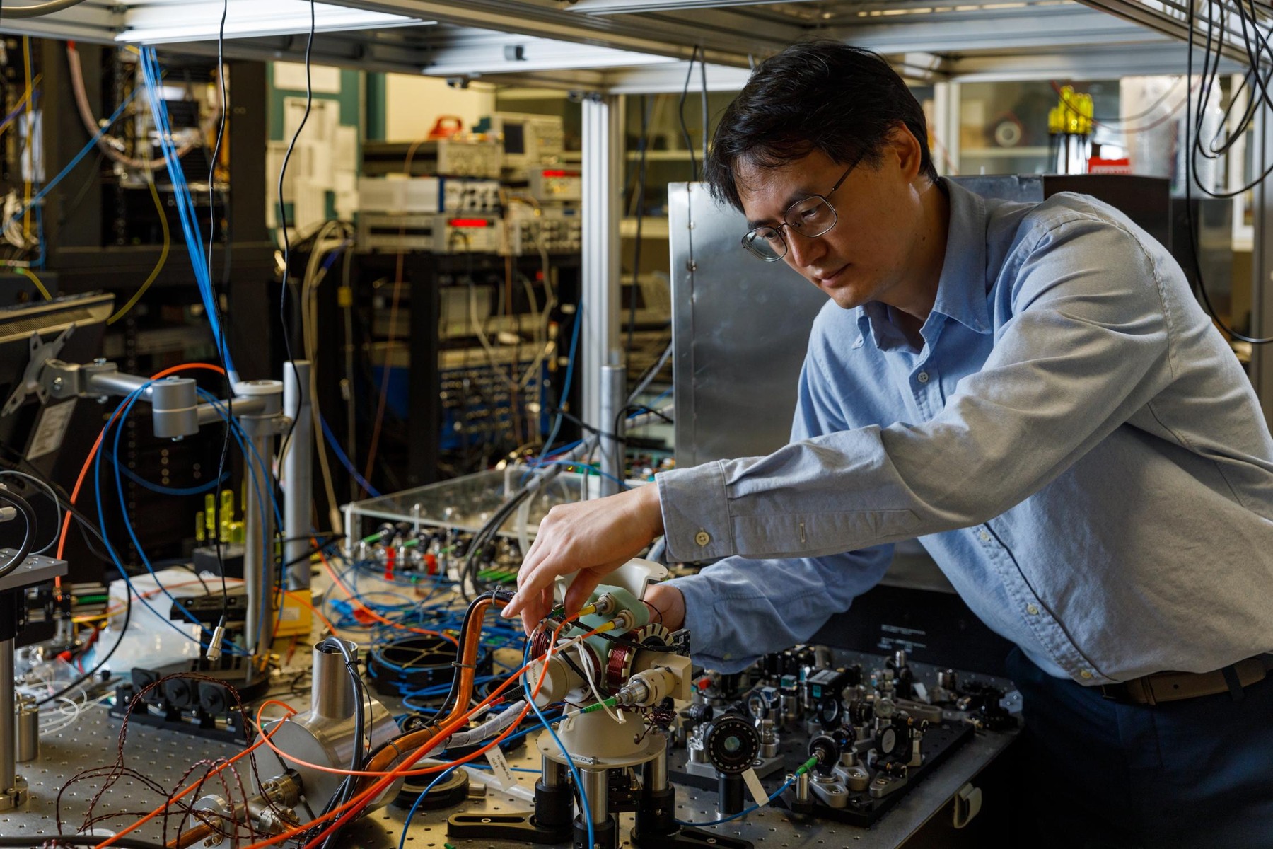 Researcher examining a compact cold-atom vacuum sensor on an optical table.