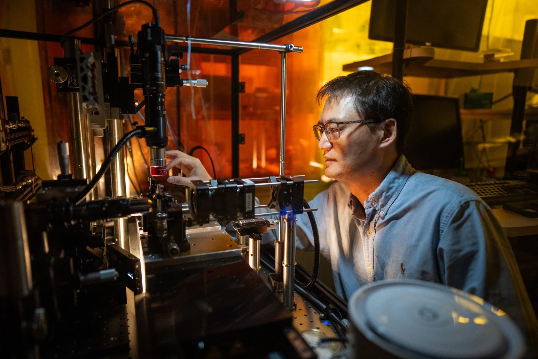 Researcher beside optical equipment and laser components in Sandia’s nanofiber laboratory.