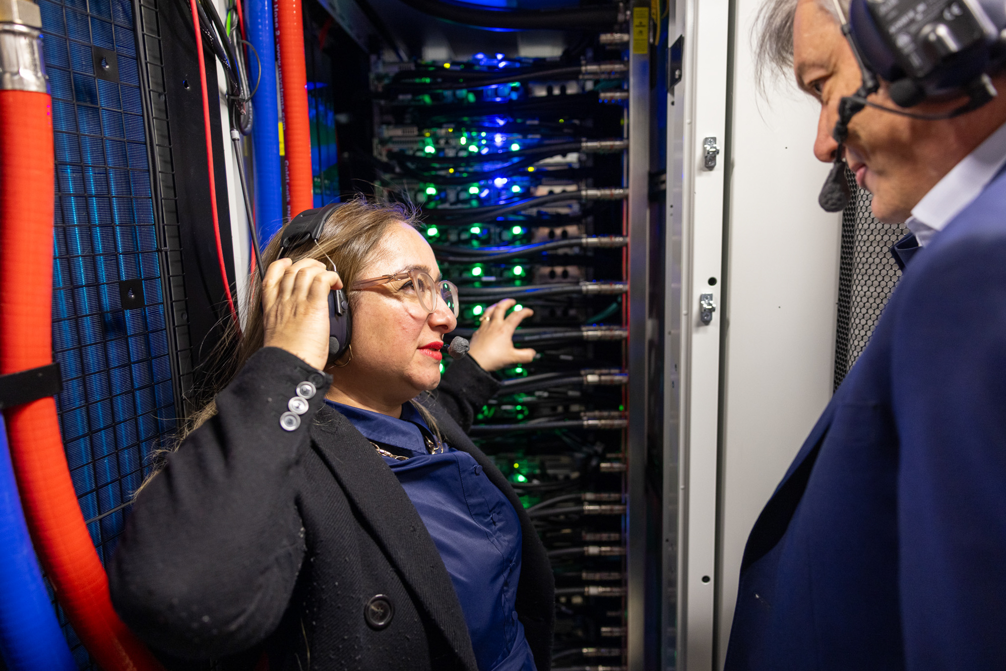 Feryal Clark wearing a headset beside illuminated server equipment during a visit to Cambridge's Dawn supercomputer.
