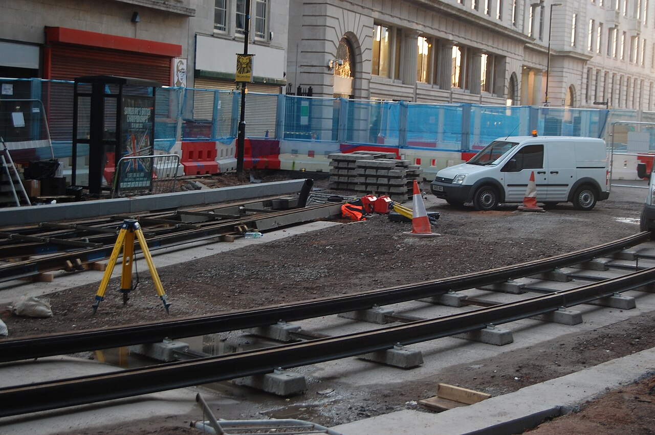Rails and concrete sleepers being installed on Upper Bull Street in Birmingham, with construction barriers and a survey tripod.