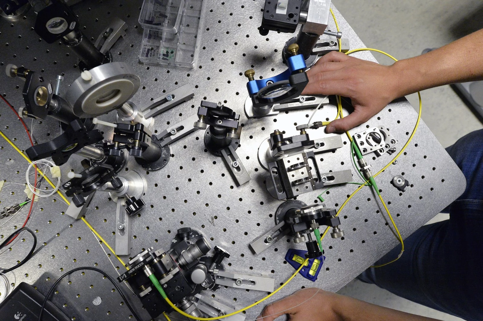 A researcher adjusts mirrors and optical mounts on a laboratory table.