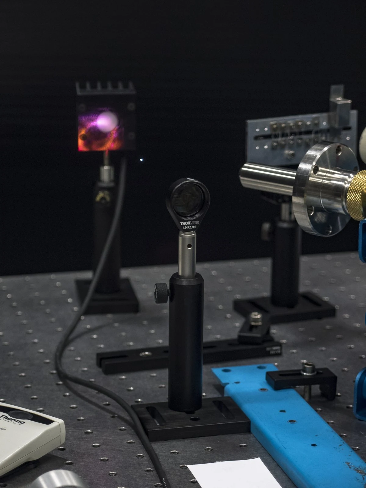 Optical mounts and a glowing spot appear along a laboratory laser setup.
