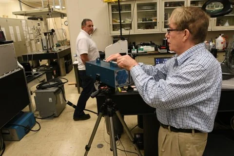 Two researchers work beside a large optical instrument in a laboratory.