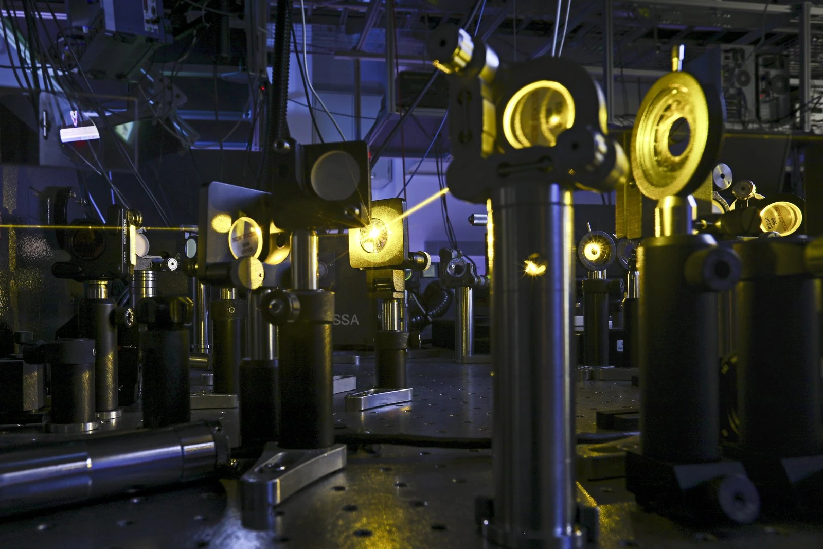 Illuminated mirrors and optical mounts fill a dark ultrafast-laser laboratory.