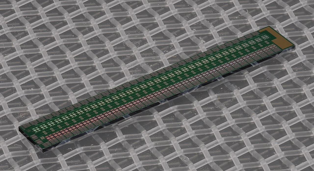 A narrow green superconducting circuit chip resting diagonally on a gray woven surface.