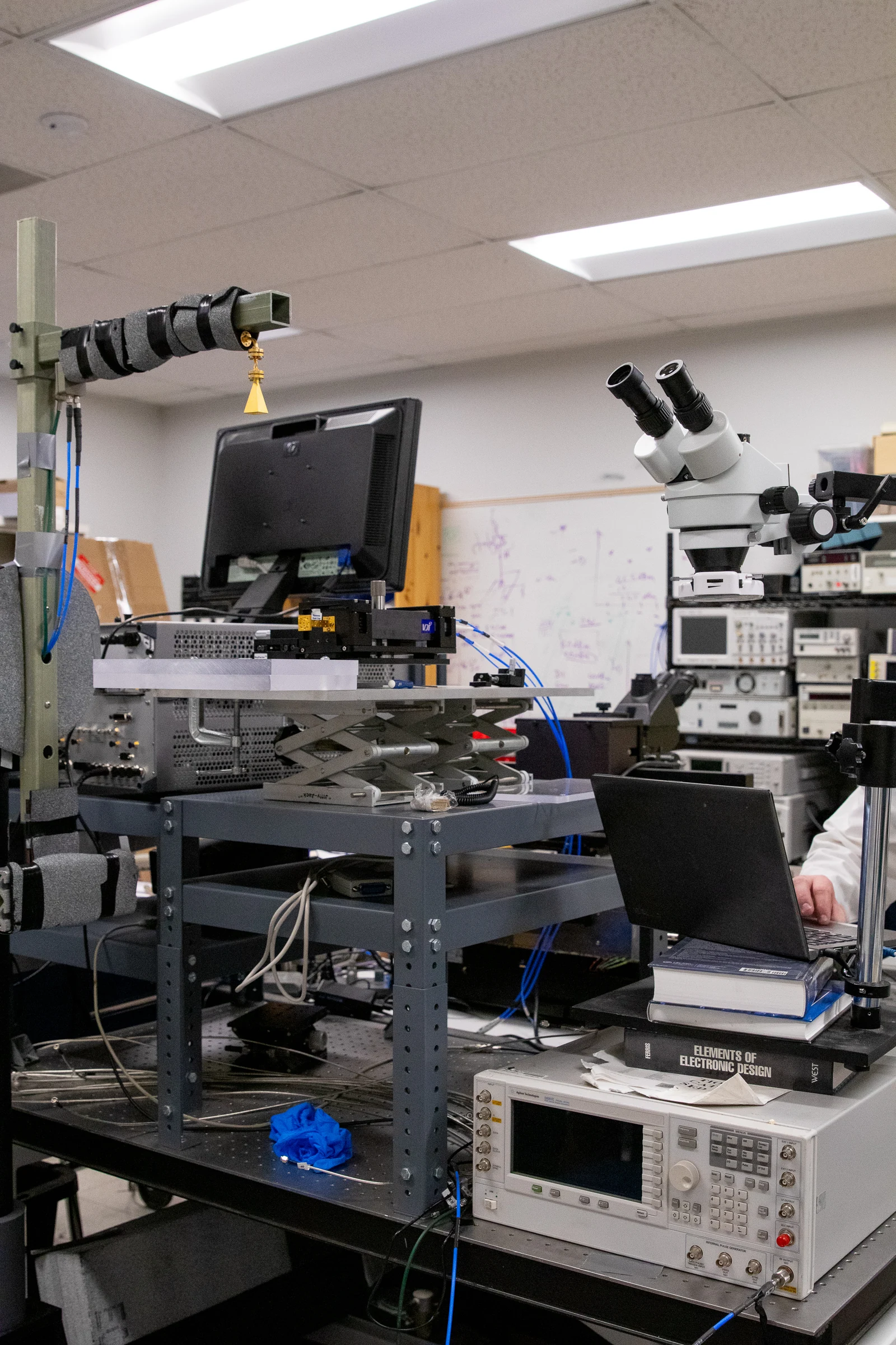 A microscope, measurement instruments and a laptop arranged around a test bench in a microwave research laboratory.