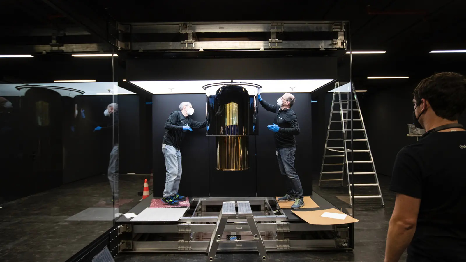 Engineers work on IBM Quantum System One inside its glass enclosure in Ehningen, Germany, with the cryogenic assembly, tools and supporting structure visible