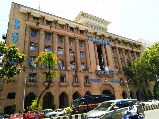 Columned facade of Bank of India's Mumbai main branch with blue bank signs and traffic in the foreground.