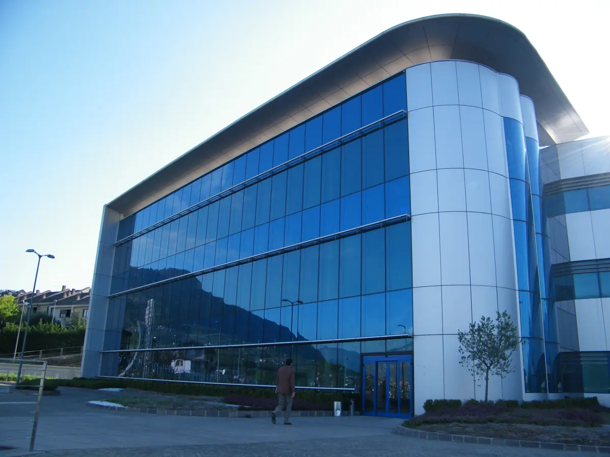 Blue-glass university science building with a curved roof and paved entrance in Povo, Trento.