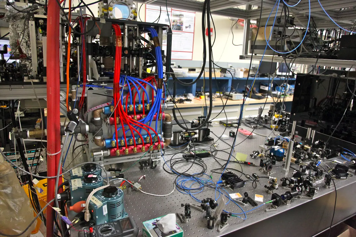 An optical table crowded with vacuum equipment, cables and red and blue tubes in a Stanford cold-atom laboratory.
