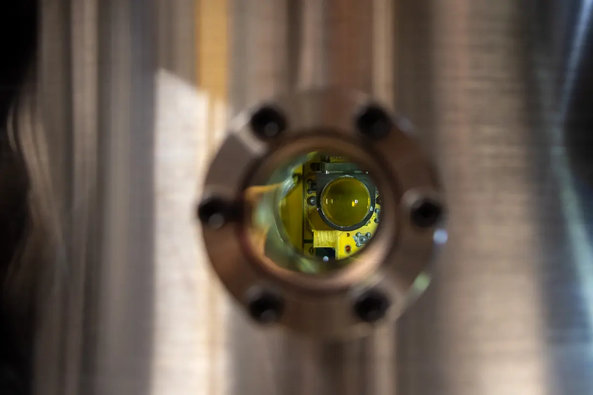 View through a circular opening in metallic laboratory equipment, with yellow-tinted components inside.