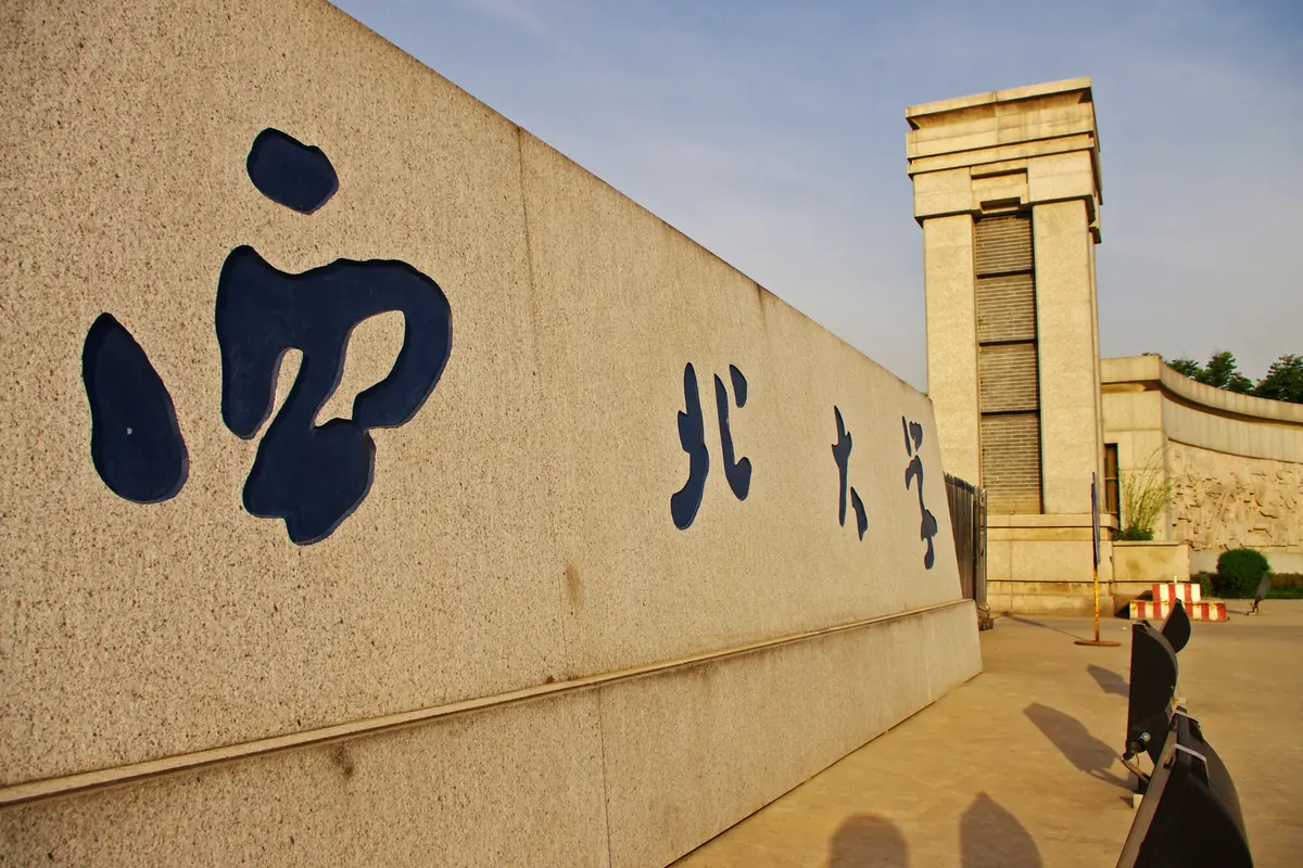 Chinese characters naming Northwest University on a stone wall beside the Chang'an campus entrance tower.