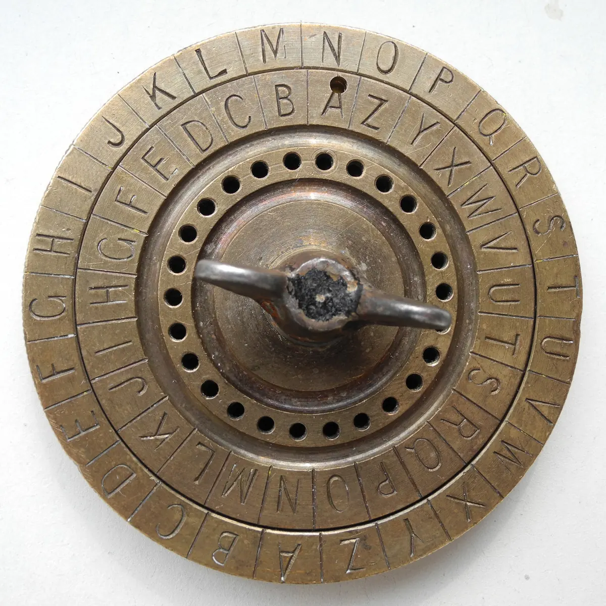 A brass cipher disc with two concentric alphabet rings and a central handle.