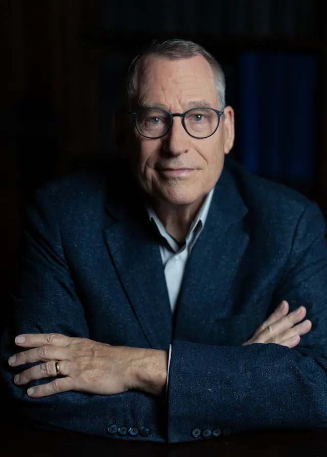 John Preskill wearing glasses and a dark jacket in a seated portrait.