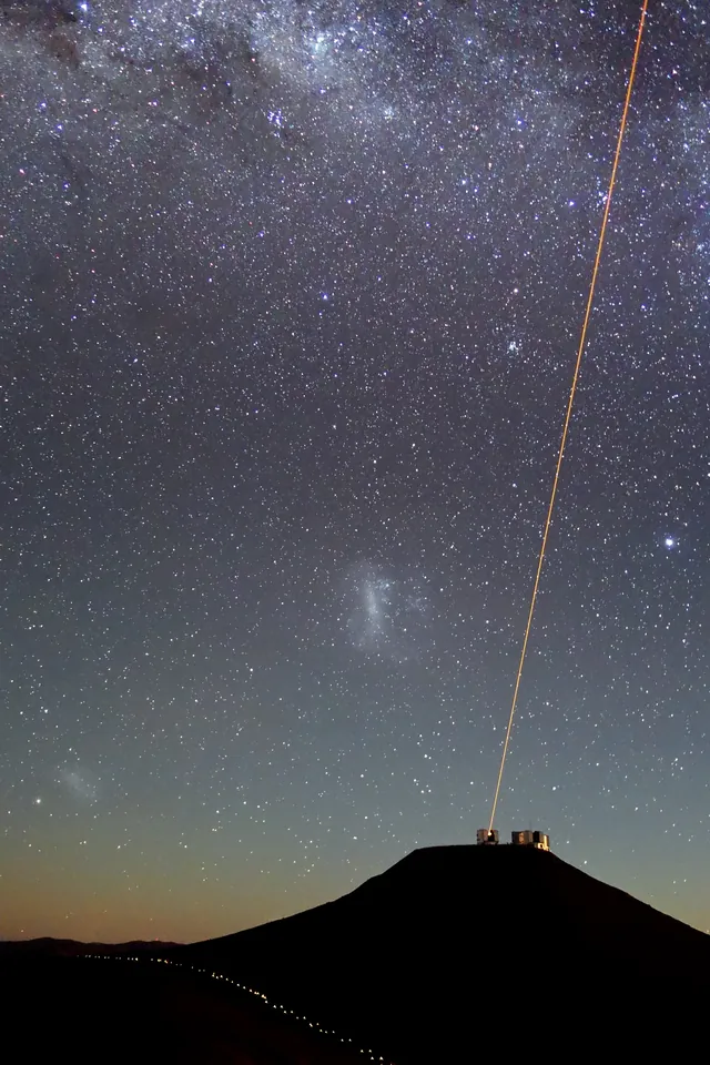 A laser guide-star beam rises from a telescope into a star-filled sky above Paranal Observatory.