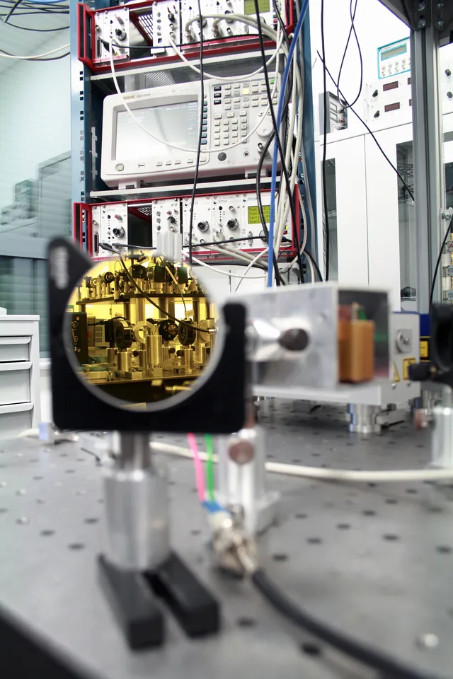 A gold mirror reflects instruments and an optical table in an atom-cooling laboratory.