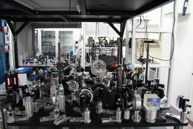 Optical mounts, lenses and a vacuum apparatus cover a laboratory table.