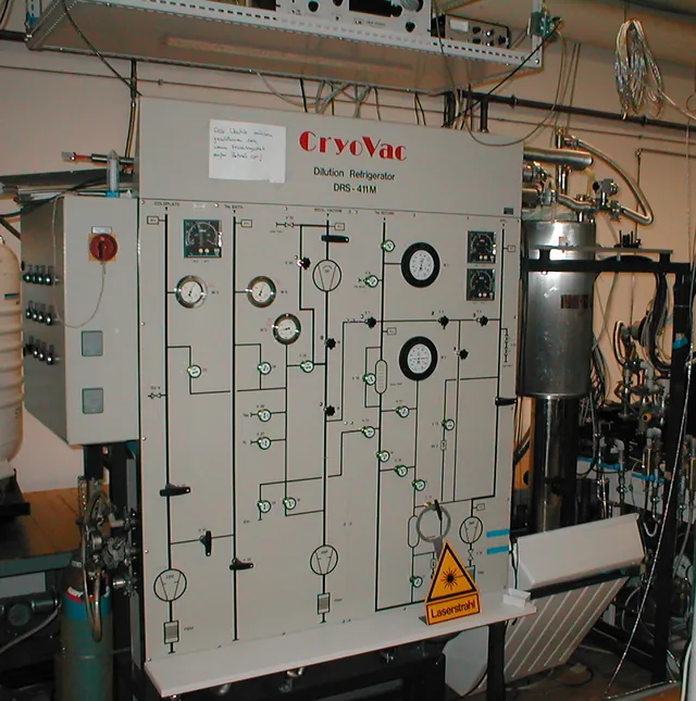 A helium dilution refrigerator installation includes a large gas-handling panel and metal plumbing.