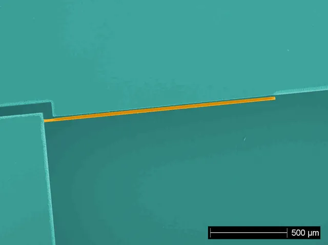 A colourized micrograph shows a narrow orange silicon cantilever beside a patterned electrode.
