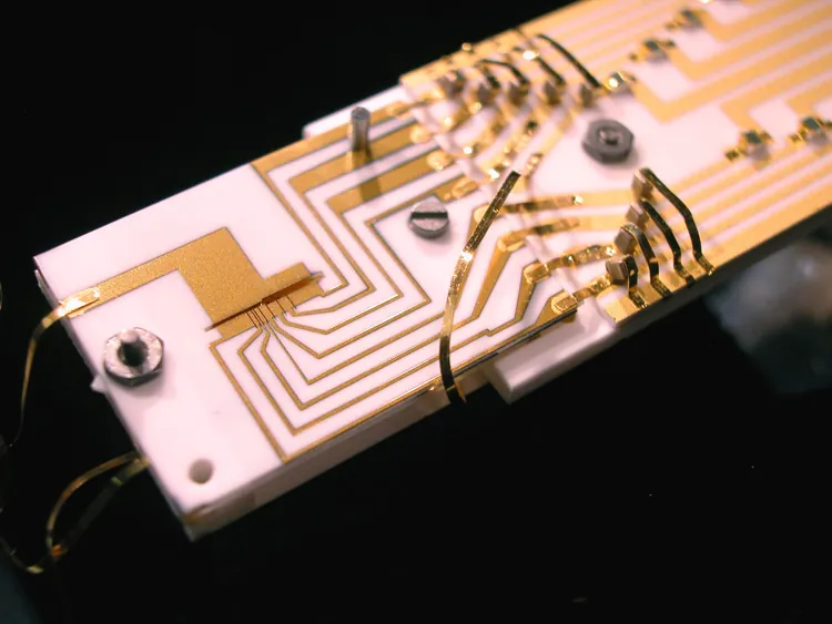 A narrow gold-coated ion-trap assembly is fixed to a board with electrical connections.