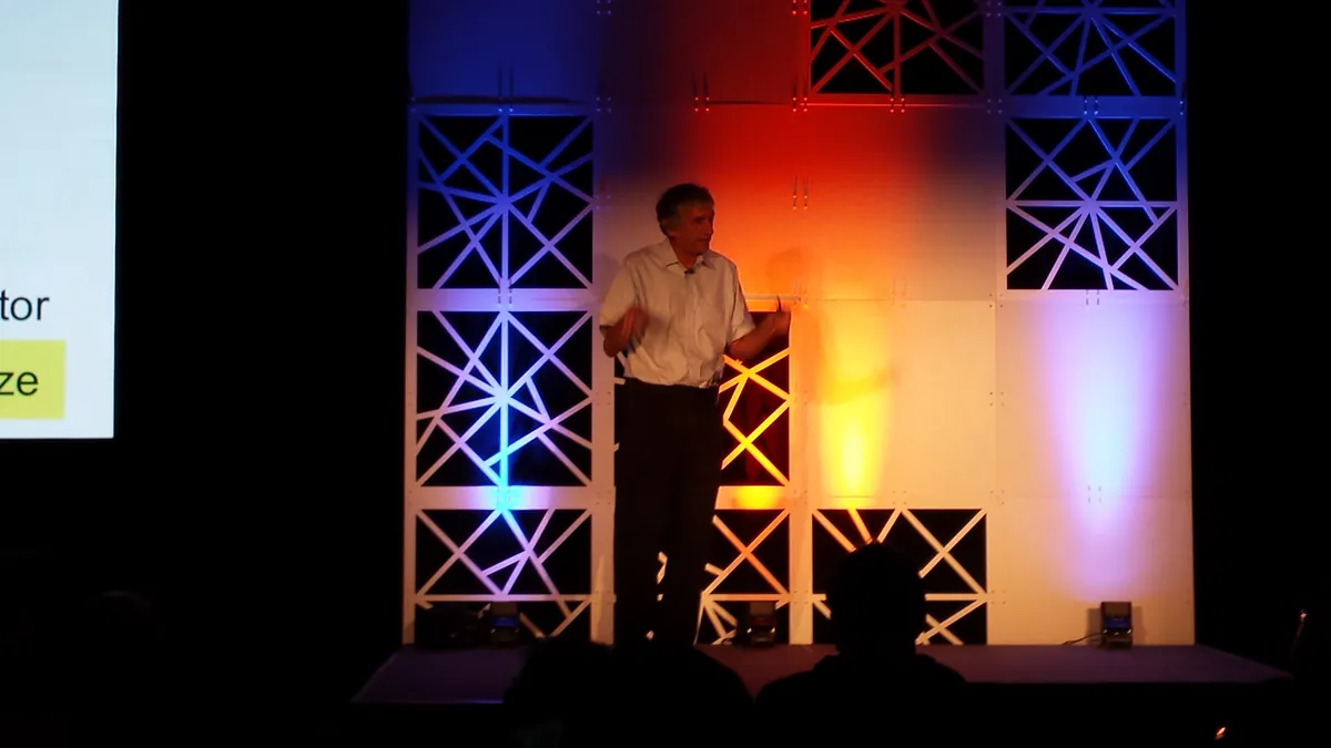 John Martinis speaks on a conference stage beside a projected presentation.
