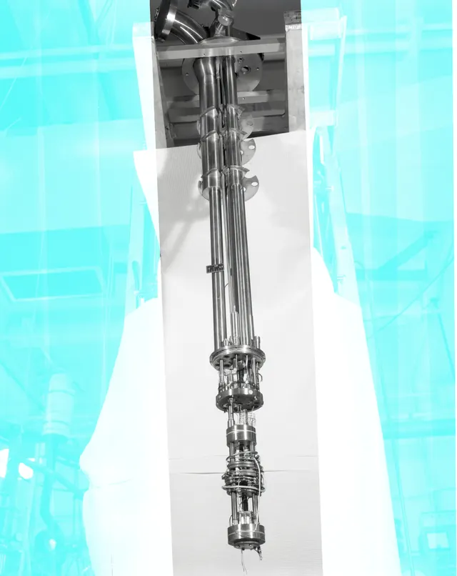 An elongated metal dilution-refrigerator insert hangs vertically in an archival laboratory photograph.
