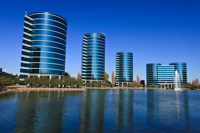 Curved glass office towers reflected in water at Oracle’s Redwood Shores campus.
