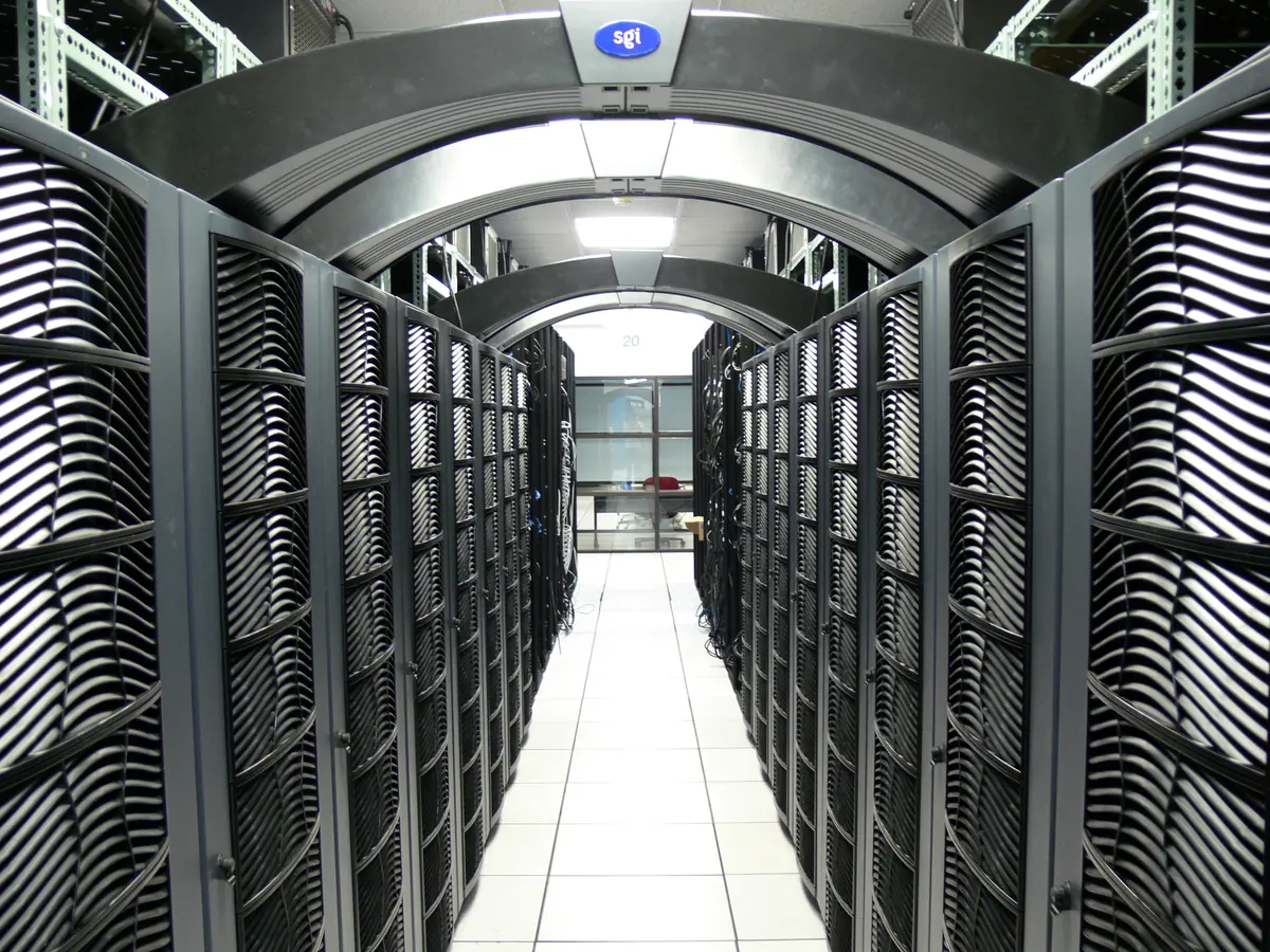 Rows of black equipment cabinets beneath curved overhead supports in a data center.