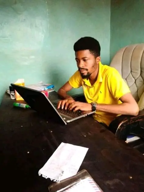 A person in a yellow shirt working on a laptop at a dark table.