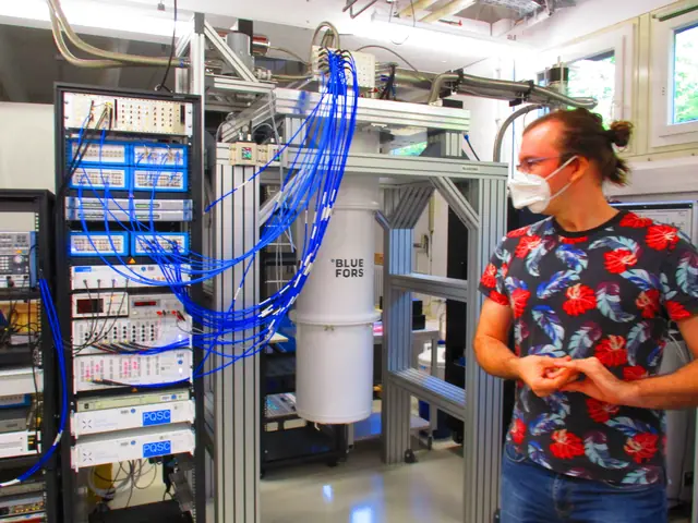 A researcher beside a cryogenic cylinder and racks of laboratory control electronics at Jülich.