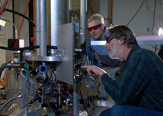Two researchers work beside the tall silver NIST-F2 atomic-clock apparatus.